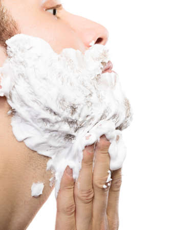 Health beauty and skin care concept. Closeup young bearded man with foam on face preparing to shave, guy shaving on whiteの写真素材