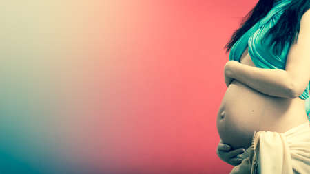 New life concept. Pregnancy, motherhood and happiness. Closeup tummy of pregnant woman wearing blue scarf on redの写真素材