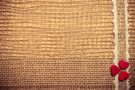 Valentines day or wedding concept. Red wooden decorative hearts lace ribbon on abstract cloth burlap background with copy space. Vintage aged toneの写真素材