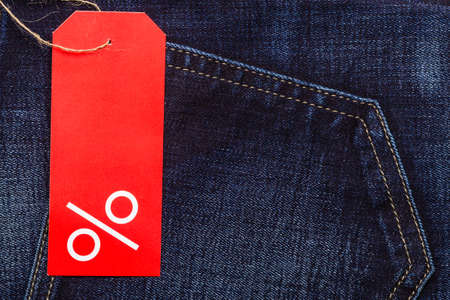 Shopping and sale concept. Closeup red label with percent sign and copy space on navy blue jeans pocket denim cotton material backgroundの写真素材