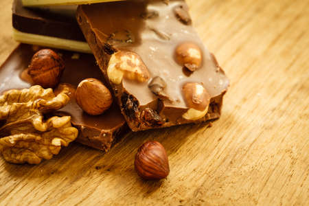 Closeup milk chocolate pieces and hazelnuts on wooden table.の写真素材