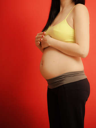 New life concept. Pregnancy, motherhood and happiness. Closeup tummy of pregnant woman on redの写真素材