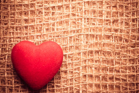 Valentines day or wedding concept. Red big heart love symbol on rustic brown bagging cloth background with copy space. Vintage aged styleの写真素材