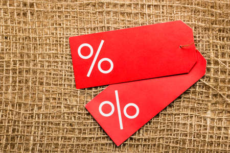 Shopping and sale concept. Two red price labels with percent sign on cloth burlap surface background. Copyspaceの写真素材