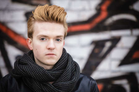 Portrait of handsome trendy man outdoor in city setting, male model stylish haircut against graffiti wallの写真素材