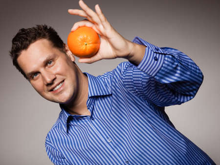 Diet and nutrition. Young smiling man holding orange tropical fruit on gray. Happy guy recommending healthy food.の写真素材