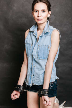 Arrest and jail. Criminal woman prisoner girl showing leather handcuffs on gray. Punishment.の写真素材