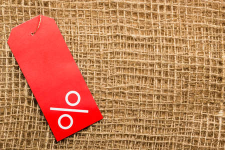 Shopping and sale concept. Red price label with percent sign on cloth burlap surface background. Copyspaceの写真素材