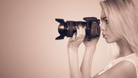 Photographer girl shooting images. Attractive blonde woman taking photos with camera. Filtered photo