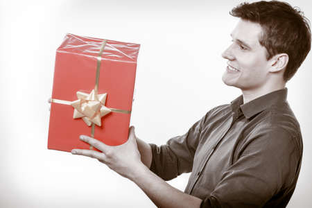 Holiday and special occasion. Young handsome man giving red present gift box with golden ribbon isolated on white. Surprise. Studio shot.の写真素材