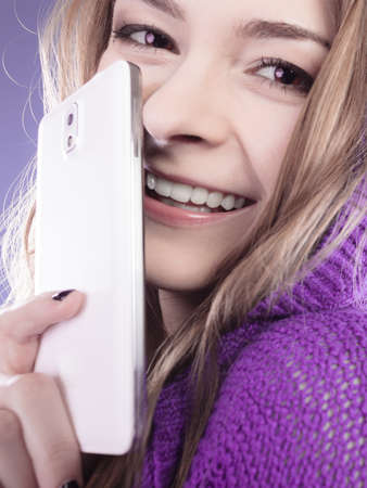 Technology and communication. Closeup young smiling woman teenage girl covering her face with mobile phone, using smartphone on violetの写真素材