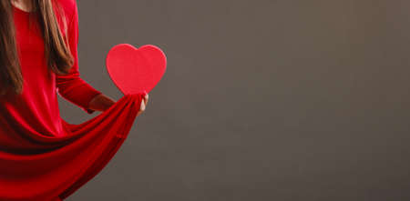 Valentines day, love, romance concept. Woman in red dress holding heart shaped gift box in hands dark gray backgroundの写真素材