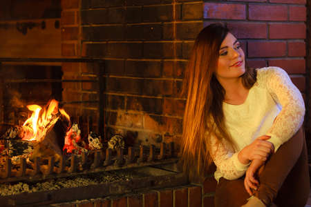 Winter at home, heating. Young woman beauty long hair girl relaxing warming up at fire fireplace. Indoor.の写真素材