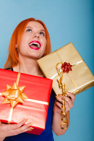 People celebrating holidays, love and happiness concept - happy joyful red hair girl with gift boxes studio shot on blue backgroundの写真素材
