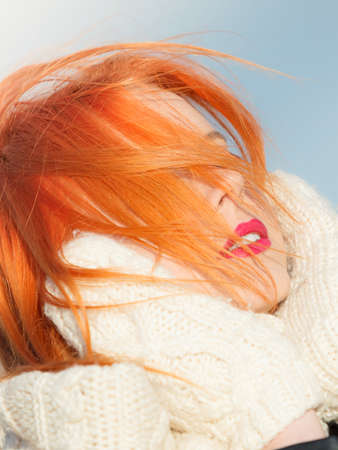 Winter fashion. Beauty redhaired head with hair blowing on wind, woman in warm clothing outdoor enjoying sunlight.の写真素材