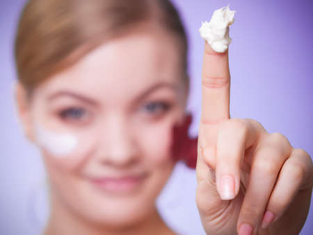 Skincare habits. Face of young woman with leaf as symbol of red capillary skin on gray. Girl taking care of her dry complexion applying moisturizing cream. Beauty treatment.の写真素材