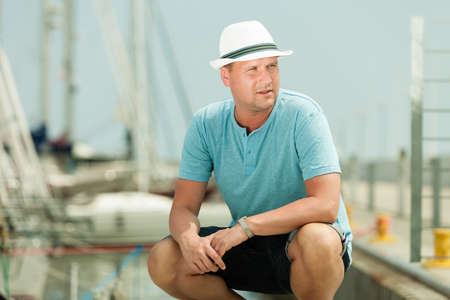 Travel tourism vacation and people concept. Fashion portrait of handsome man on pier against yachts...
