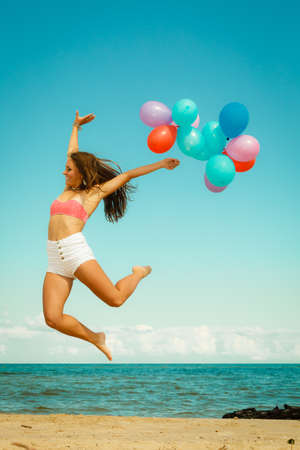 Summer holidays, celebration and lifestyle concept - beautiful woman teen girl jumping with colorful balloons outside on beachの写真素材