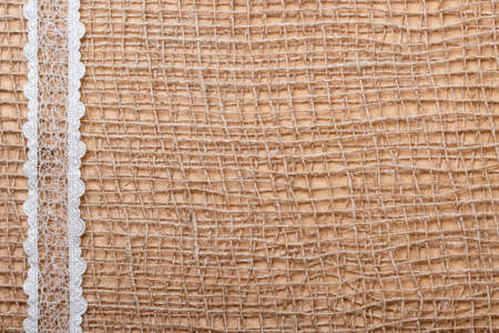 White lace ribbon on brown mesh material, natural burlap background