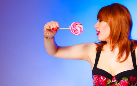 Candies under control. Snack concept. Studio shot. Pretty smiling girl with lollipop in hand on blue background.の写真素材