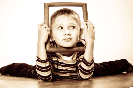 Portrait of little funny blonde boy child holding photo frame framing his face looking into the corner studio shotの写真素材