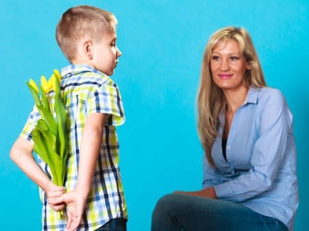Holiday mother's day concept. Rear view little boy with bunch of yellow tulips behind back preparing...