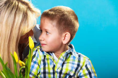 Boy celebrating mother's day. little child lad giving flowers yellow tulips to his mom mother studio shot on blueの写真素材