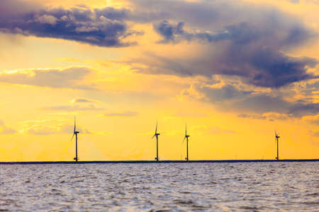 wind turbines power generator farm for renewable energy production along coast baltic sea near Denmark at sunset or sunrise. Alternative green energy ecology.の写真素材