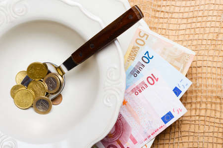 Cost of living, price of food and eating wealth concept. Euro money on kitchen table, plate spoon with coins and banknoteの写真素材