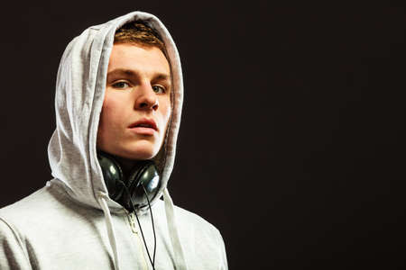 Headshot young handsome hooded man with headphones listening to music black backgroundの写真素材
