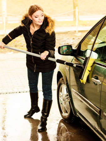 Auto wash. Young attractive blonde woman washing the dirty car on open airの写真素材