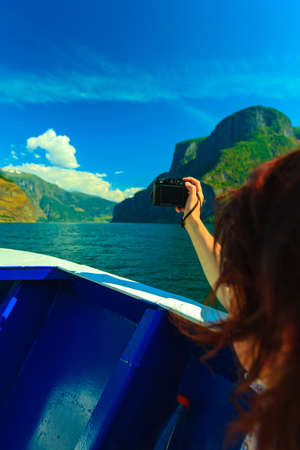 Tourism vacation and travel. Woman tourist taking photo with camera, view from deck of ship on fjord Sognefjord in Norway, Scandinavia.の写真素材