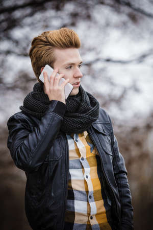 Technology and communication. Young fashion man talking on mobile cell phone using smartphone outdoorの写真素材