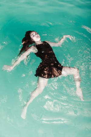 Sensuality and sexuality of women. Sexual posing woman in black dress in water. Indoor.の写真素材