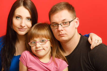 cute family of three face closeup portrait. Woman man and child little girl on redの写真素材
