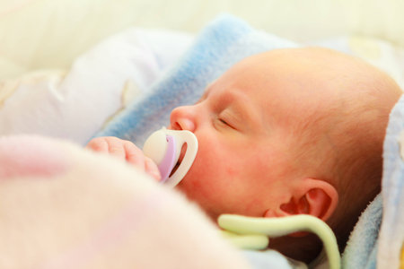 Closeup little newborn baby girl 24 days sleeping with dummy in mouth