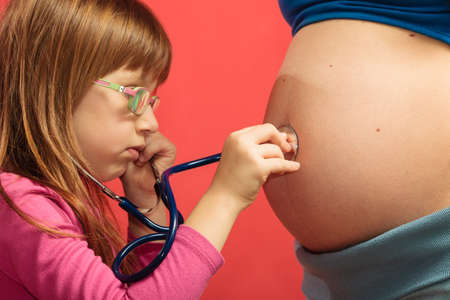 Pregnant woman with her daughter. Little girl excited about her coming sibling - listening to mother's tummyの写真素材