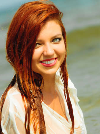 Vacation. Sensual girl wet cloth in water on the coast. Redhair woman having fun relaxing on the...