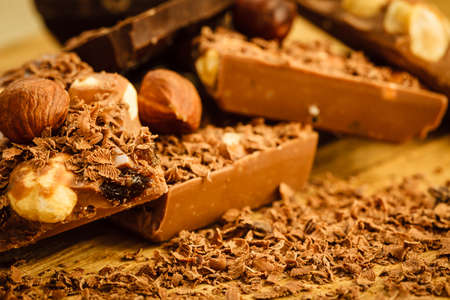 Closeup milk chocolate pieces hazelnuts and shavings curls on wooden table.