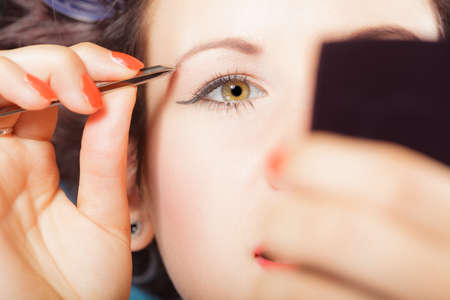Closeup part of face, woman plucking eyebrows depilating with tweezers. Girl tweezing eyebrows.の写真素材