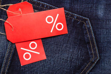 Shopping and sale concept. Closeup two red labels with percent sign and copy space on navy blue jeans pocket denim cotton material backgroundの写真素材