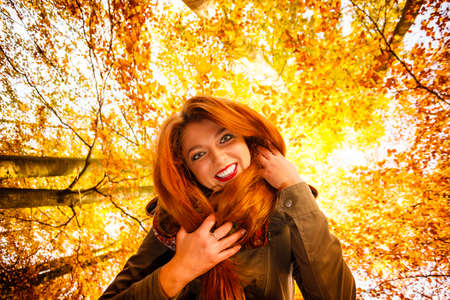 Season and happy people concept. Unusual low angle view of young happy woman in autumn park. Beauty redhaired girl relaxing walking outdoorの写真素材