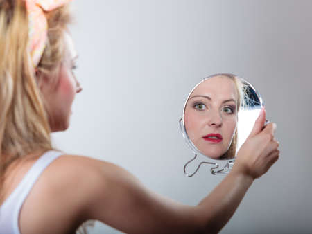 pin up beautiful blonde fashion girl in hairband looking at the mirror retro styling , studio shot gray backgroundの写真素材