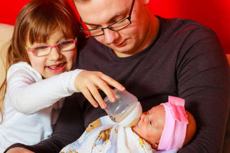 Parenting family concept. Happy young father with his daughter feeding together newborn baby girl...