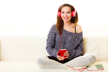People leisure relax concept. Woman casual style red big headphones listening music mp3, sitting on couch at home relaxingの写真素材