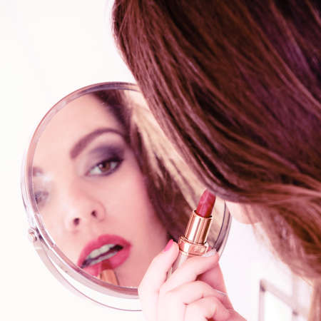 Applying make up concept. Beautiful woman with red lipstick in front of mirror. Indoor.の写真素材