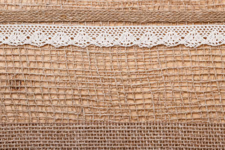 Lace and jute bagging ribbon on brown mesh material, natural burlap backgroundの写真素材