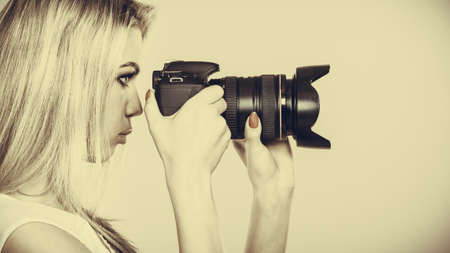 Photographer girl shooting images. Attractive blonde woman taking photos with camera. Filtered photo