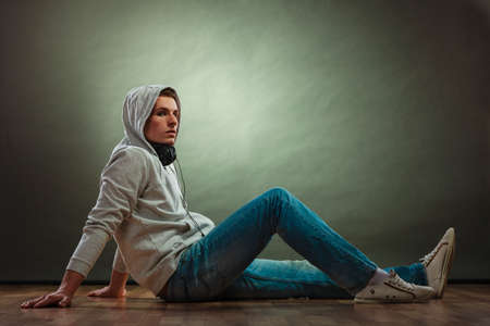Music passion youth concept. Serious hooded man teen boy with headphones sitting daydreaming on...
