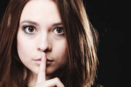 Secret woman finger on lips. Teen girl showing hand silence sign, saying hush be quiet on blackの写真素材